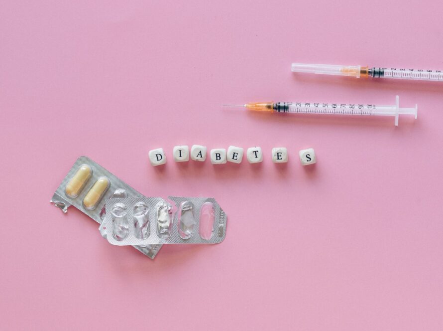 Flat lay of diabetes medication symbolized with pills and syringes on a pink background.