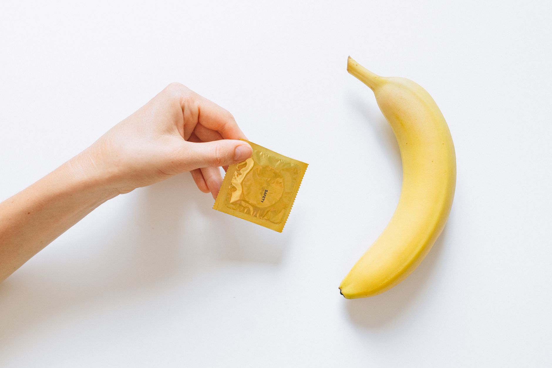 A hand holding a condom next to a banana on a white background, symbolizing safe sex education.